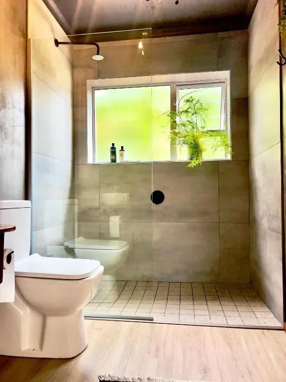 Modern bathroom with walk-in shower, toilet, and garden views through window