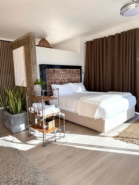 Bright modern bedroom with queen bed, brown upholstered headboard, and large windows