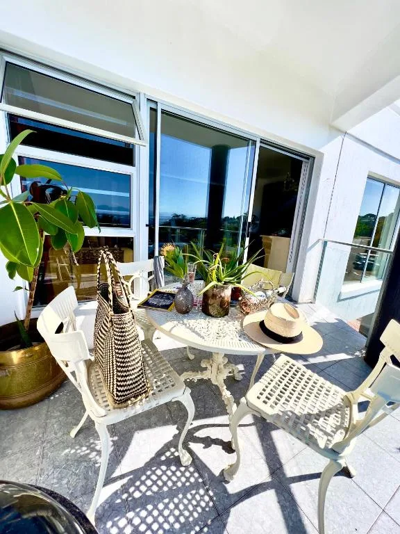 Sunny outdoor patio with white chairs, round table, and garden views
