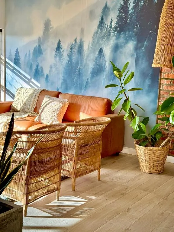 Bright lounge with woven chairs, orange leather sofa, forest mural, potted plant