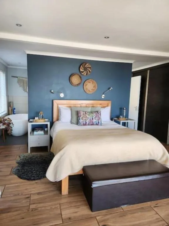 Bright bedroom with blue accent wall, wooden bed frame, cream bedding, and woven wall art