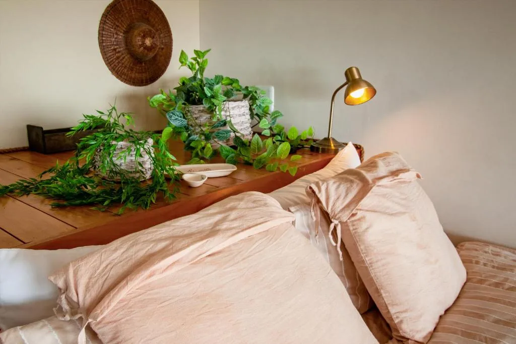 Bedroom with neutral bedding, wooden desk, potted plants and brass lamp