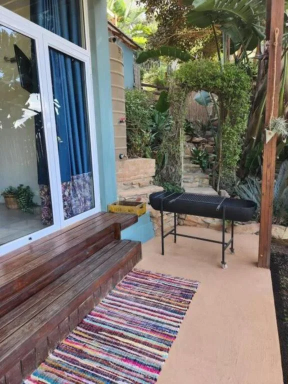 Covered patio area with wooden bench and seating, surrounded by lush greenery