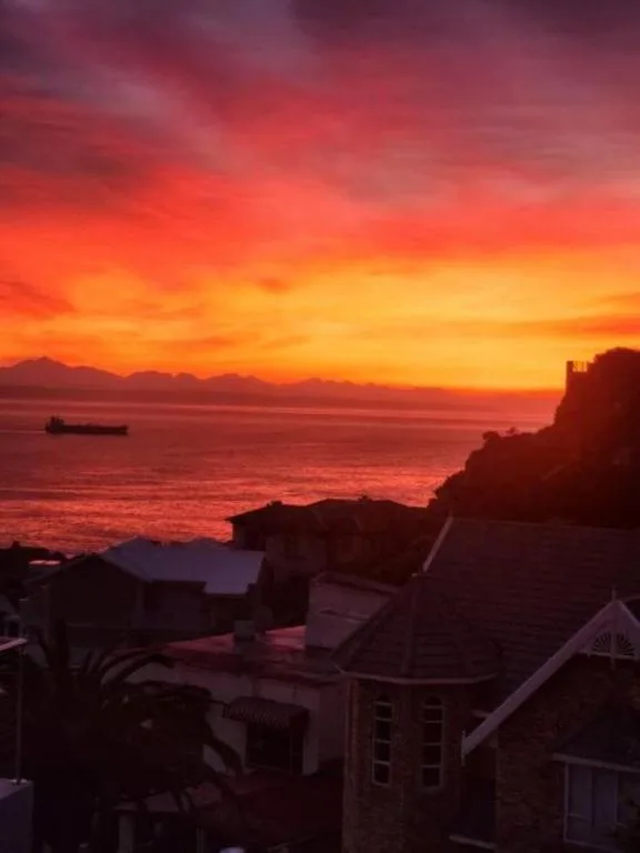 Stunning sunset over Mossel Bay with ocean, mountains, and silhouetted coastal buildings