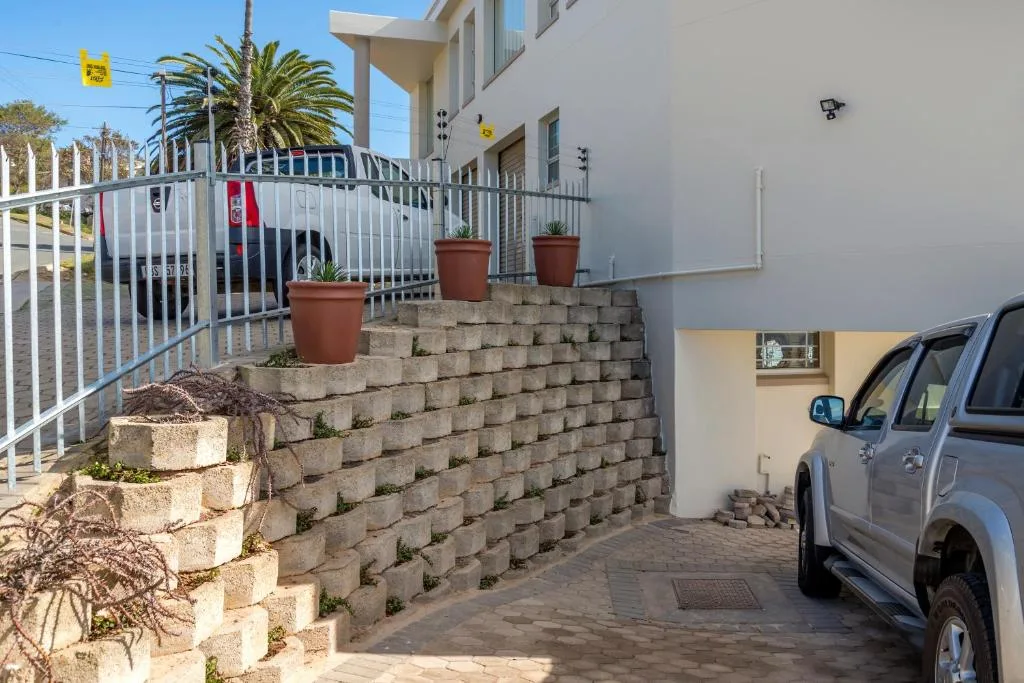 Modern white apartment building entrance with driveway, parked vehicle, and landscaping