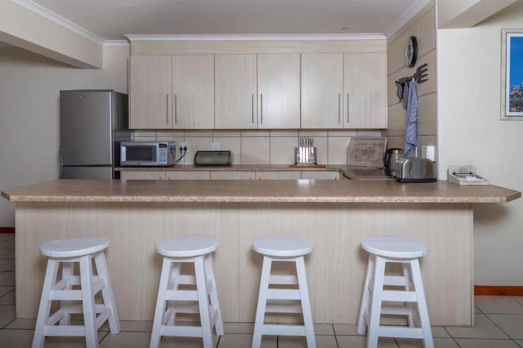 Modern kitchen with light cabinetry, granite countertop, and four white bar stools