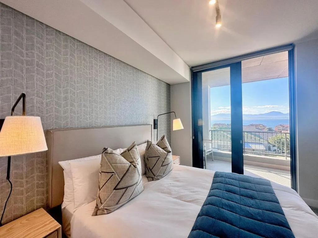 Modern bedroom with ocean and mountain views through glass doors