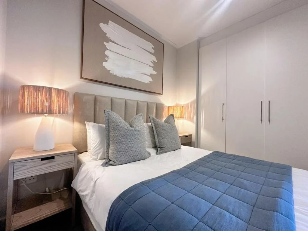 Modern bedroom with queen bed, gray upholstered headboard, blue quilt, and bedside lamps