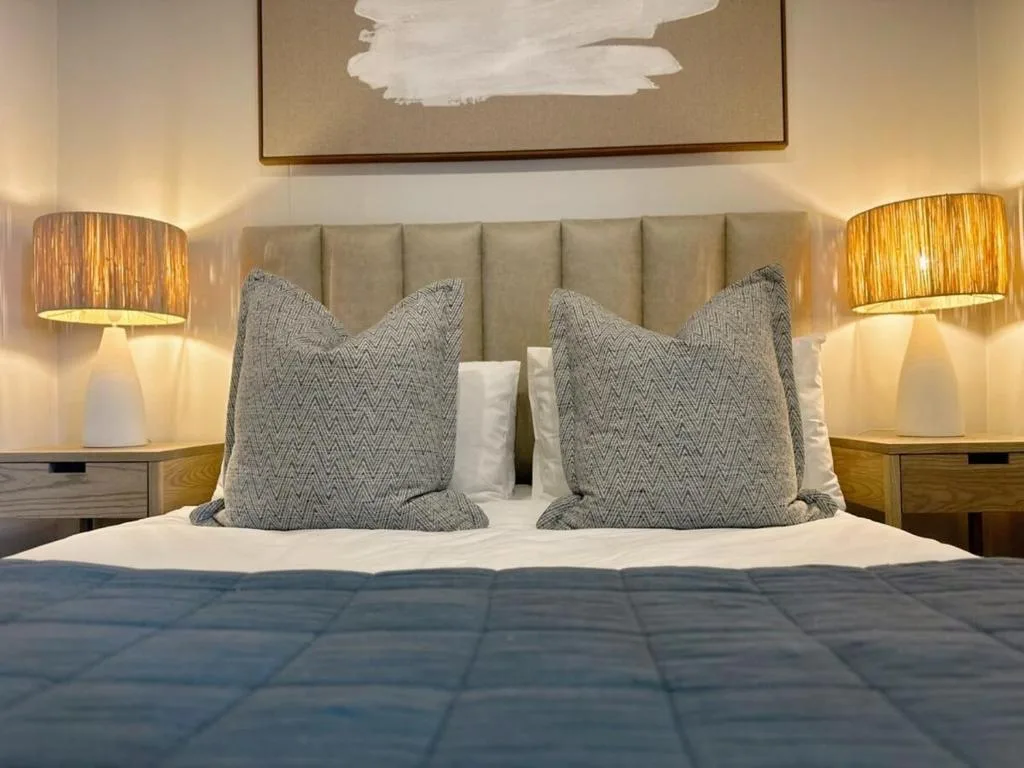 Modern bedroom with upholstered headboard, patterned pillows, and brass table lamps