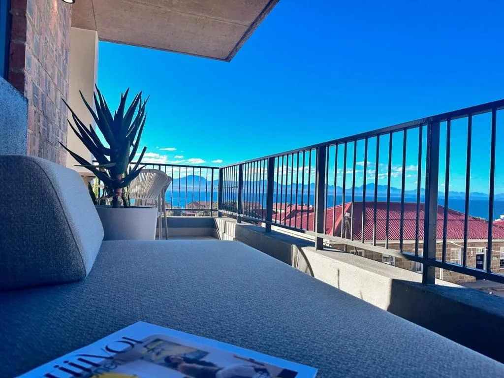 Covered balcony with ocean and coastal town views, potted plants, seating