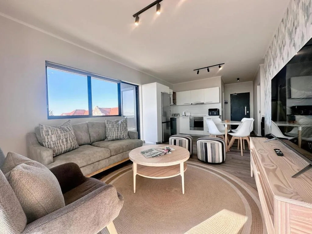Modern lounge with gray sofa, armchair, coffee table, and kitchen view