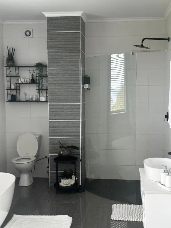 Modern bathroom with gray tile shower, white walls, toilet, and decorative shelving