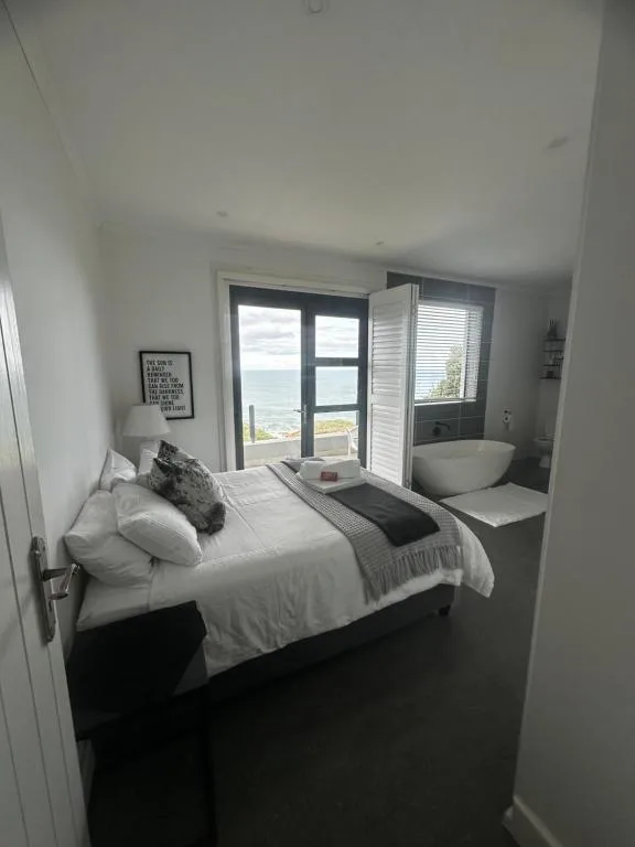 Bright bedroom with bed, ocean view through glass doors, and modern bathroom