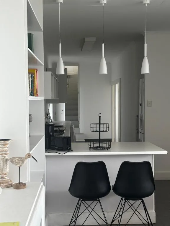 Modern kitchen with white counter, black chairs, pendant lights, and shelving