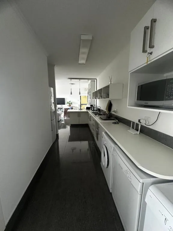Modern galley kitchen with white cabinetry, stove, microwave, and washing machine