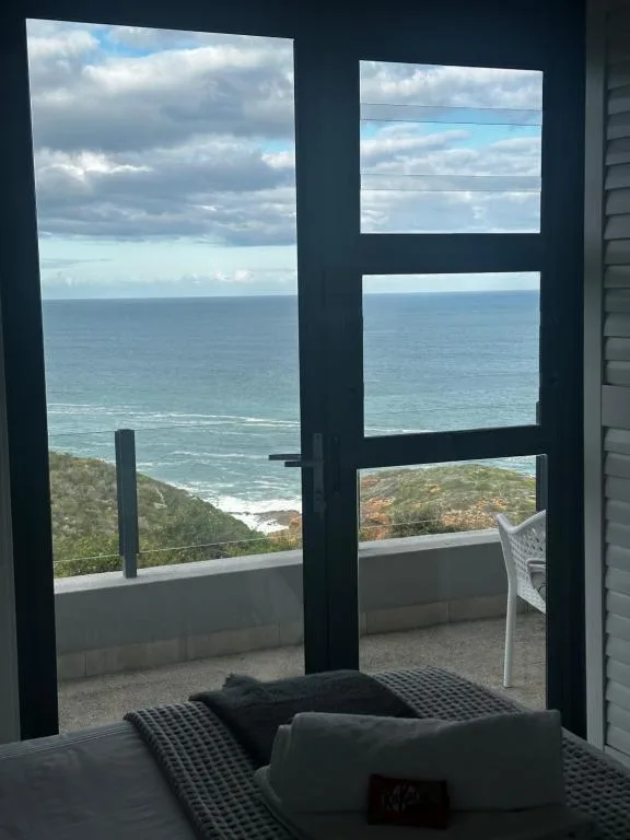 Ocean and coastline vista through large black-framed glass doors from bedroom