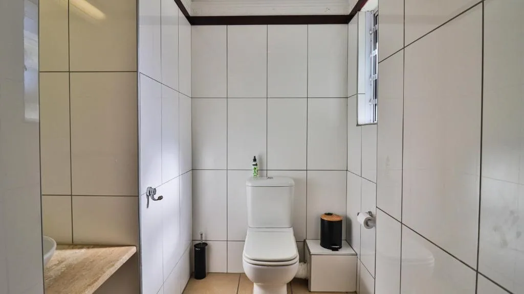 Clean white-tiled bathroom with toilet, sink, and shower enclosure