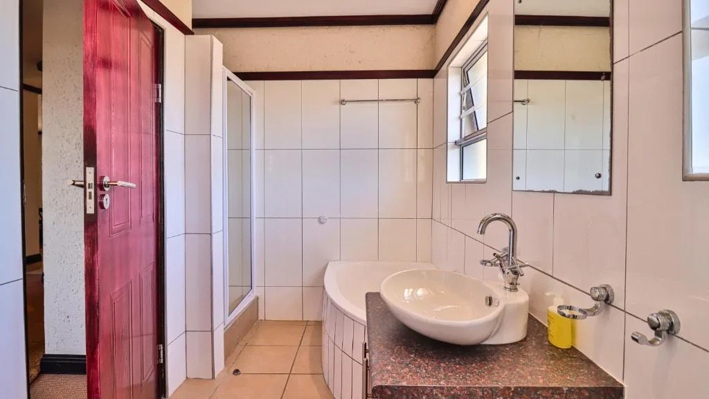 Spacious bathroom with pedestal sink, shower enclosure, mirrors, and red door