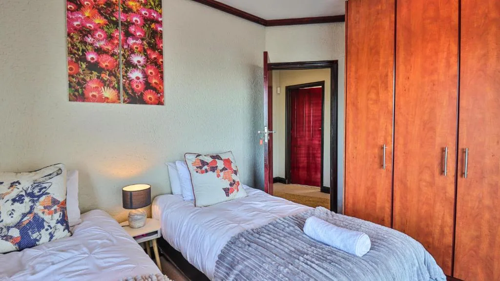 Twin bedroom with floral artwork, wood wardrobe, and red door access