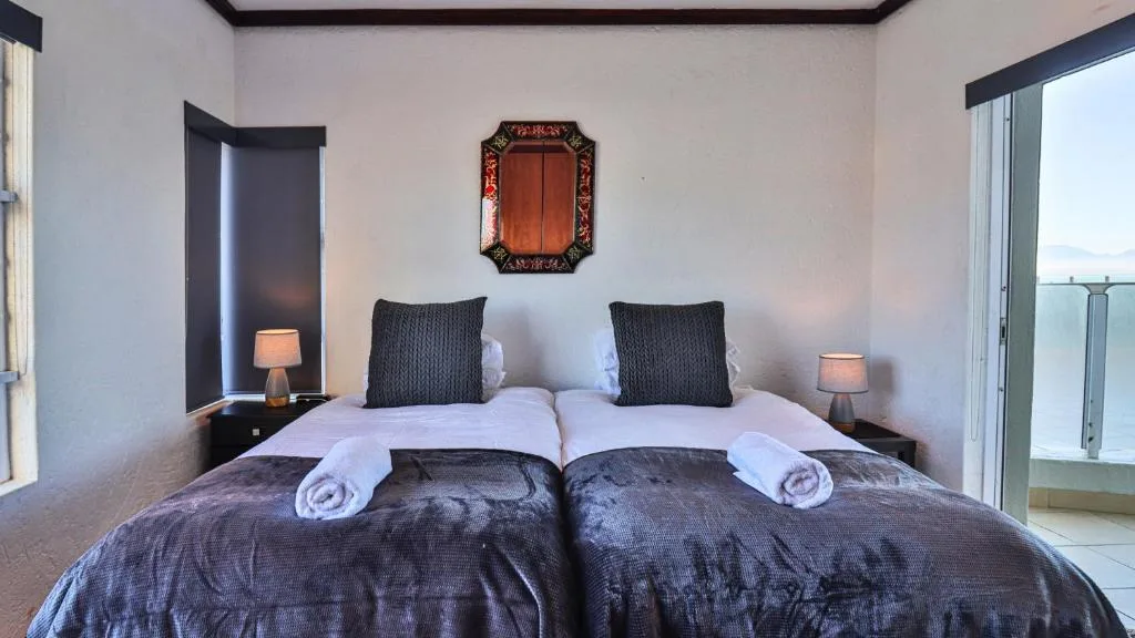 Modern bedroom with twin beds, dark bedding, and ocean view through glass doors
