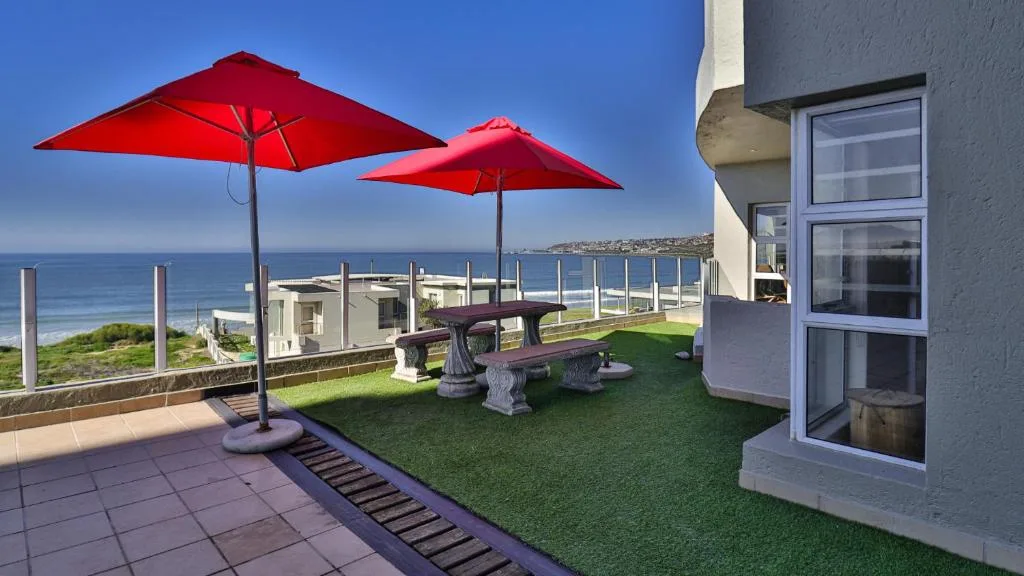 Oceanfront deck with red umbrellas, picnic table, and coastal views