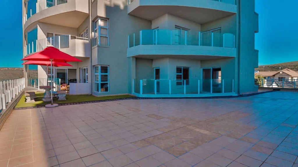 Large paved patio with red umbrella and modern blue building facade