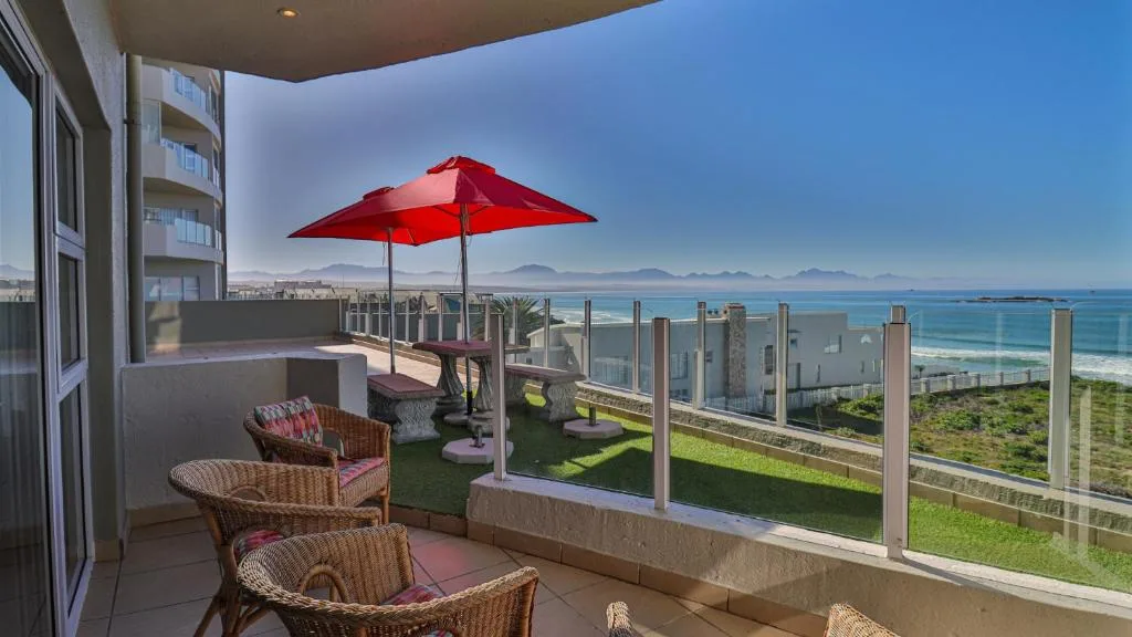 Seaside balcony with red umbrella, wicker chairs, panoramic ocean and mountain views