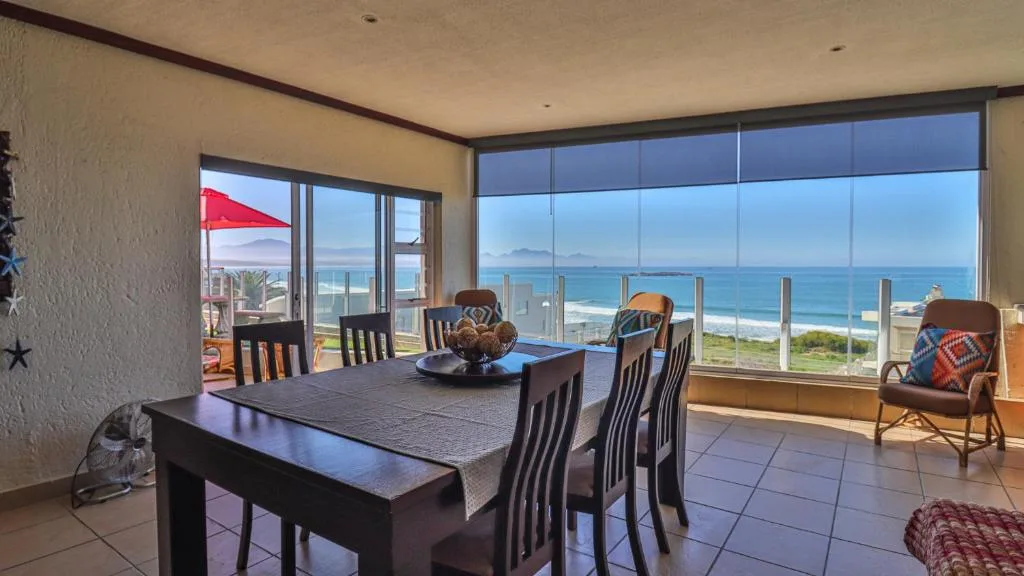 Dining table with ocean view through large windows and coastal scenery beyond