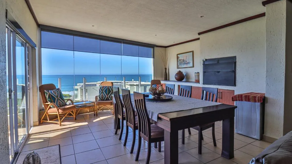 Dining area with table and chairs overlooking ocean view through large windows