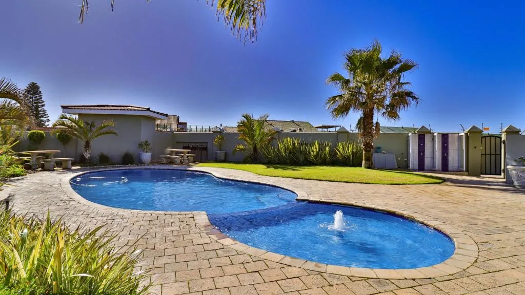 Two curved swimming pools with fountains, surrounded by paved deck and palm trees