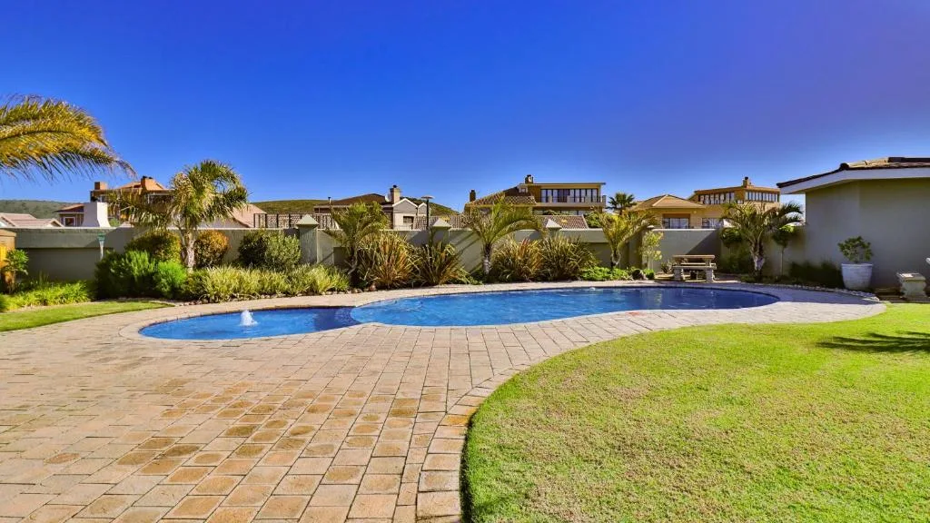 Large swimming pool with paved deck surrounded by manicured gardens and properties