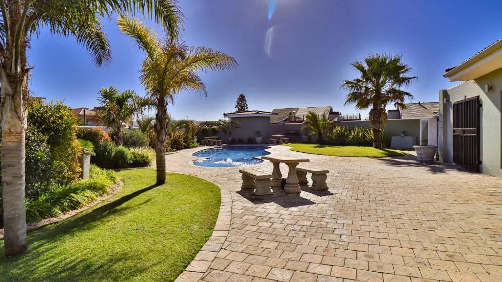 Swimming pool surrounded by manicured gardens and palm trees with patio seating