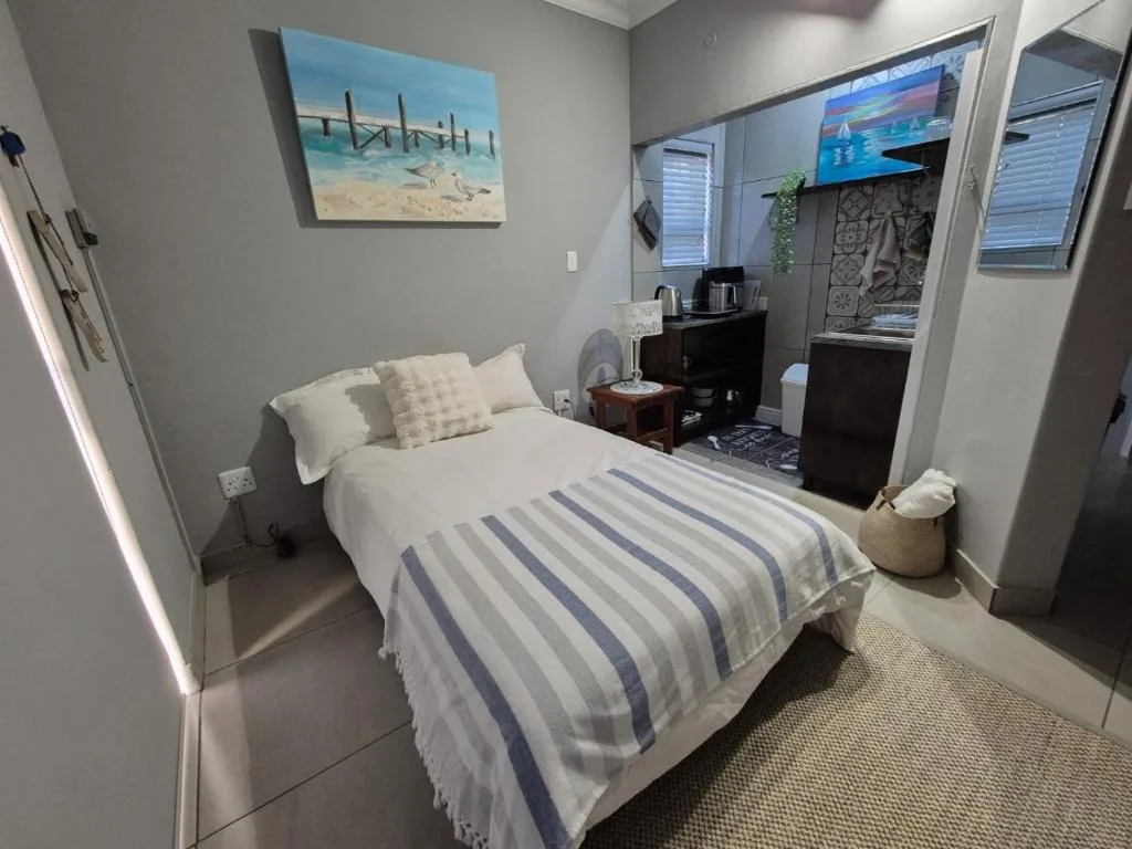 Modern bedroom with striped bedding, coastal artwork, and en-suite bathroom visible