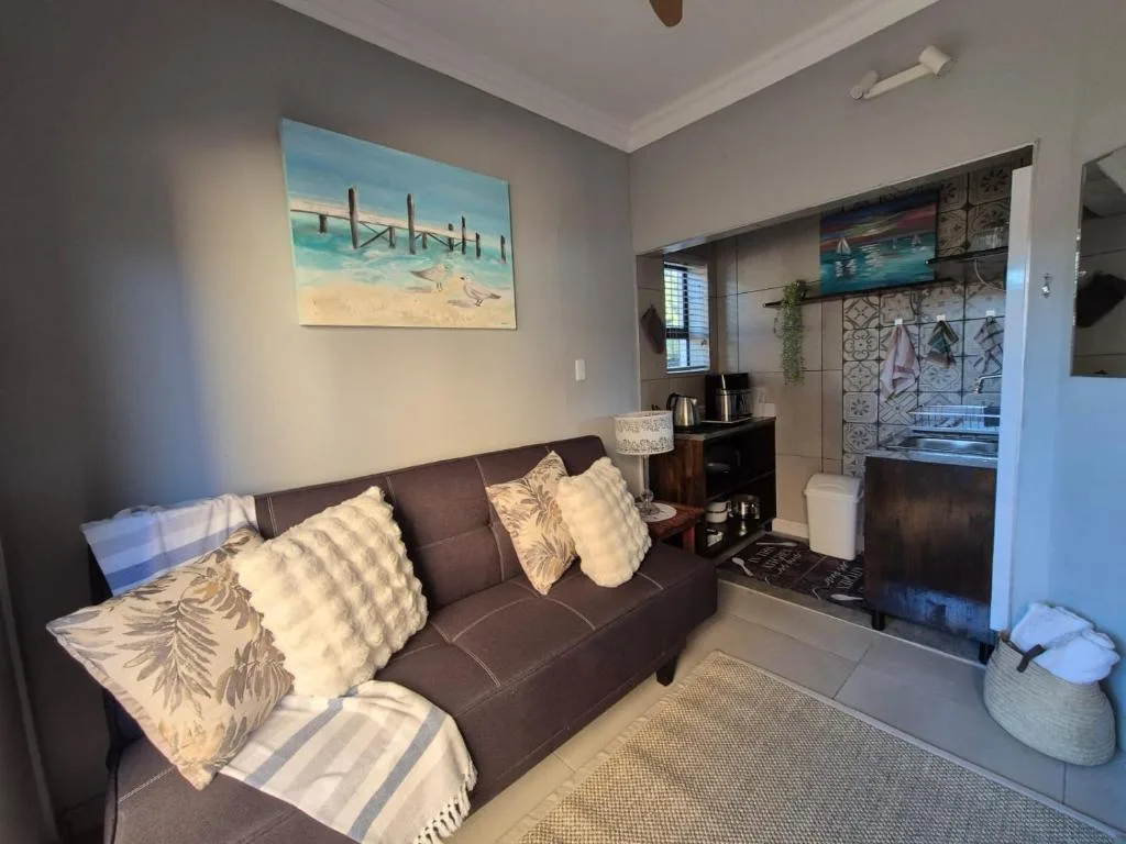 Cozy lounge with brown sofa, decorative pillows, and beach artwork on walls