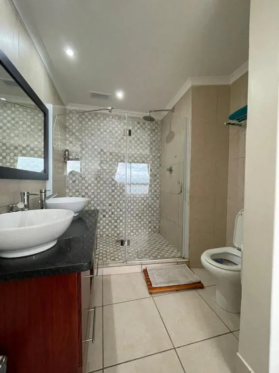 Modern bathroom with dual vanity sinks, glass shower enclosure, and toilet