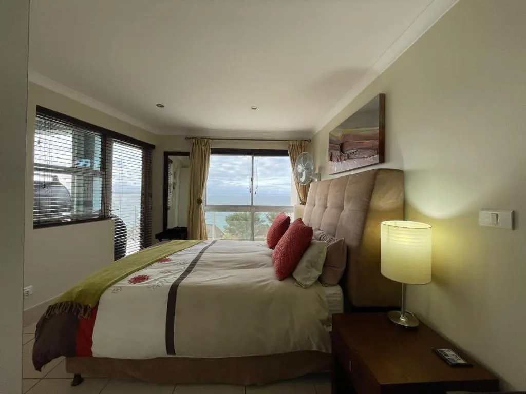 Bright bedroom with queen bed, ocean view through sliding doors, and bedside lamp