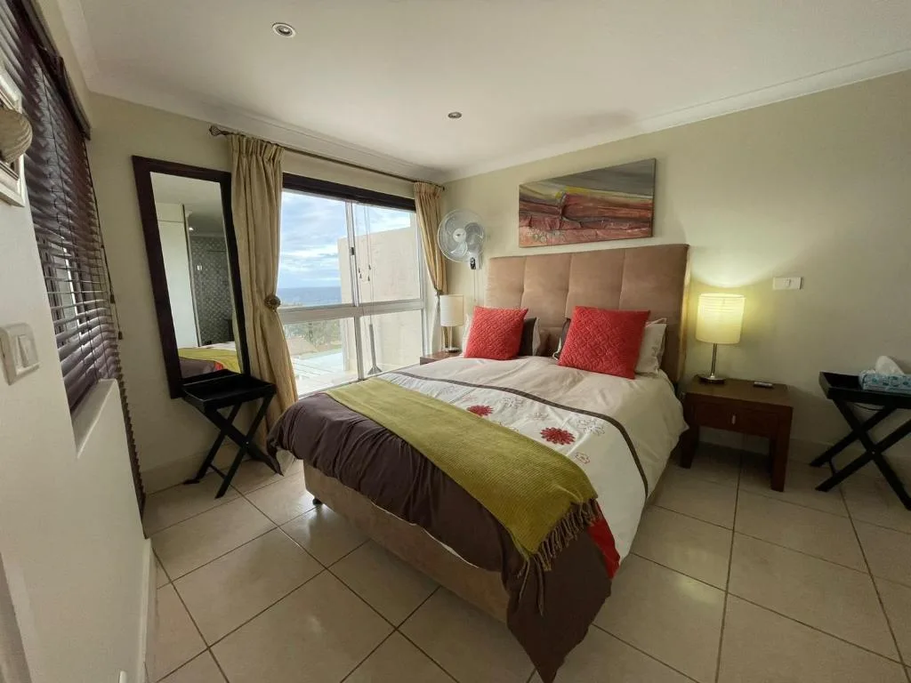 Bright bedroom with double bed, ocean view balcony, and coastal landscape