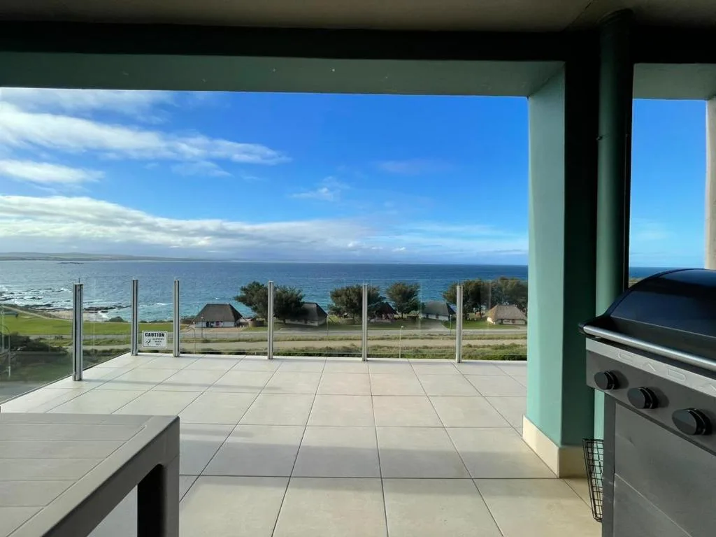 Expansive coastal deck with ocean views, glass railing, and braai grill