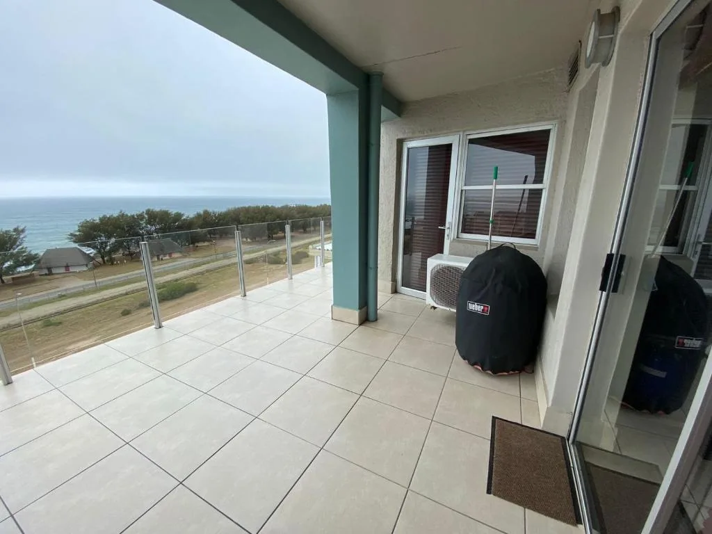 Spacious tiled balcony with ocean and coastline views, glass railing, braai grill