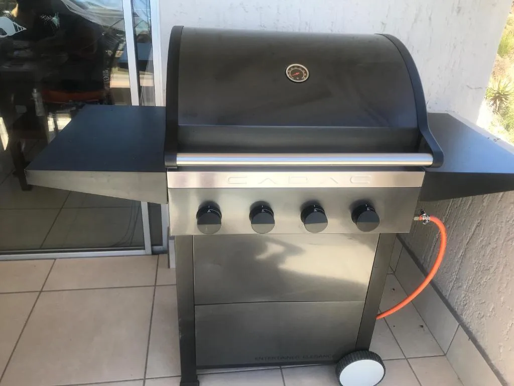 Stainless steel four-burner gas braai grill on outdoor patio area