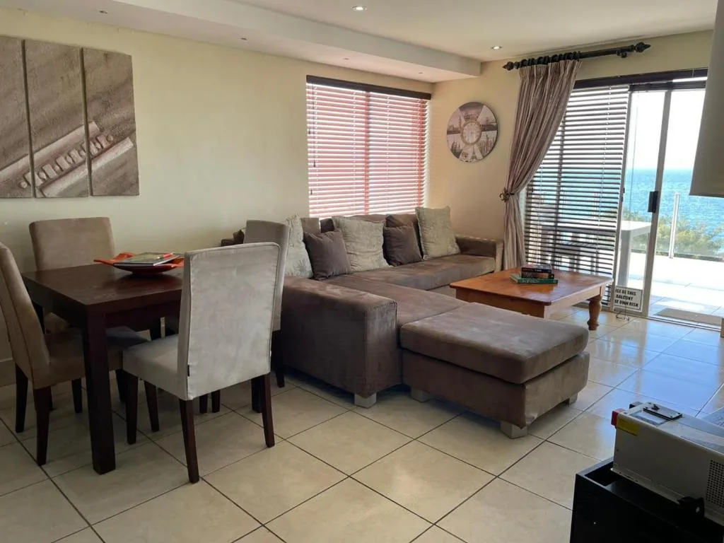 Modern lounge with brown sofa, dining table, ocean view through sliding doors