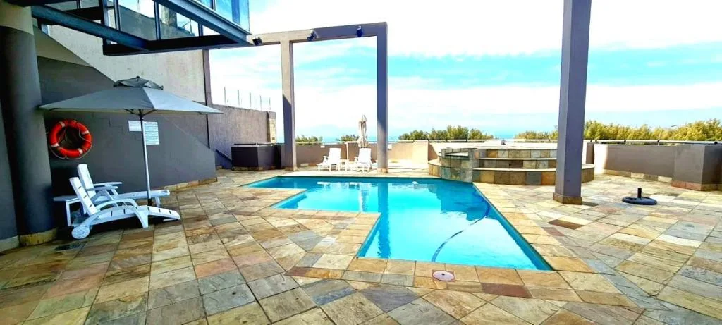 Rectangular swimming pool with bright blue water on tiled deck overlooking ocean