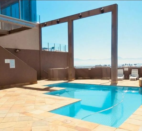 Bright blue swimming pool on sunny deck with coastal views