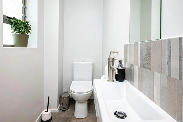 Modern bathroom with white toilet, sink, mirror and tiled walls