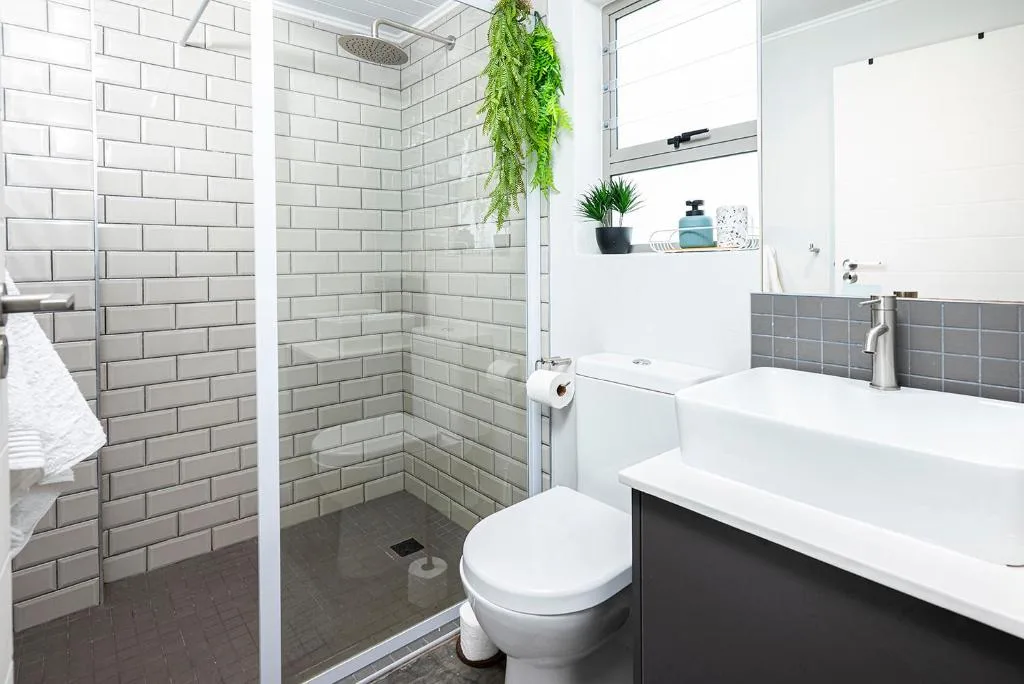 Modern bathroom with subway tile shower, white vanity, and green plant decor