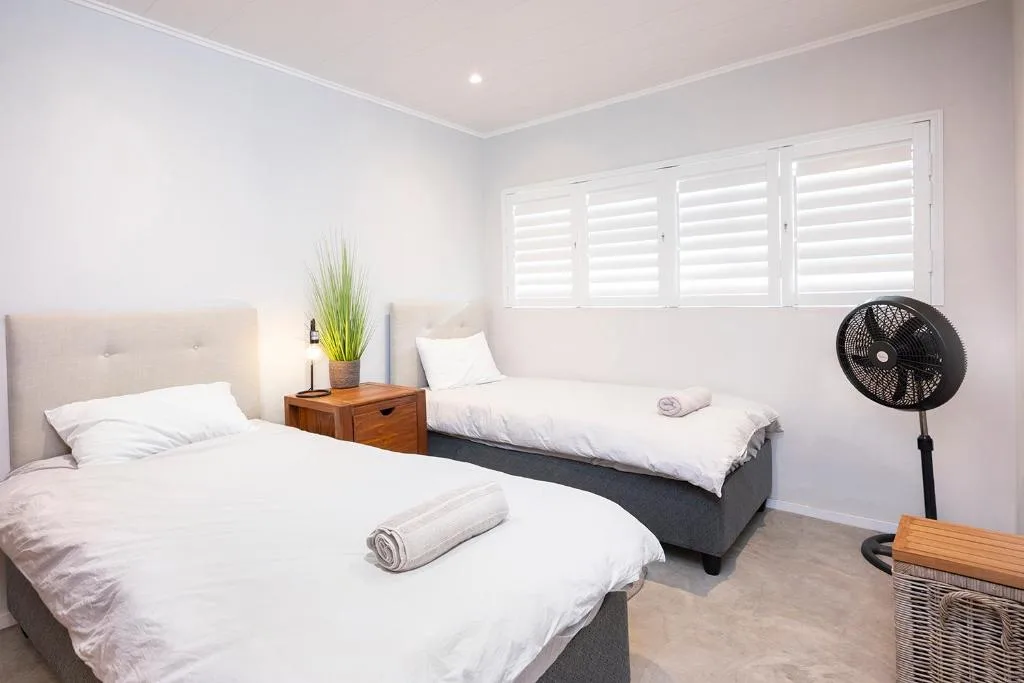 Bright twin bedroom with white bedding, wooden nightstand, and plantation shutters