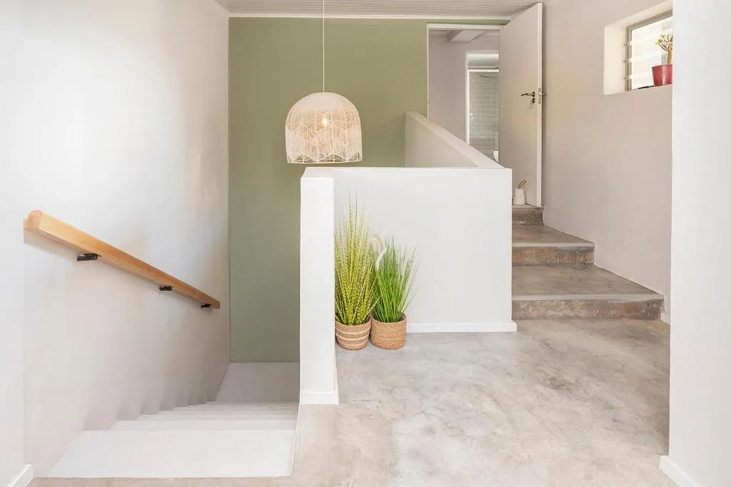 Modern entryway with sage green wall, pendant light, wooden railing, potted plants