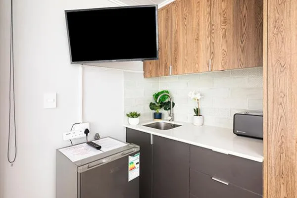 Modern kitchenette with dark cabinetry, white countertop, and wall-mounted TV
