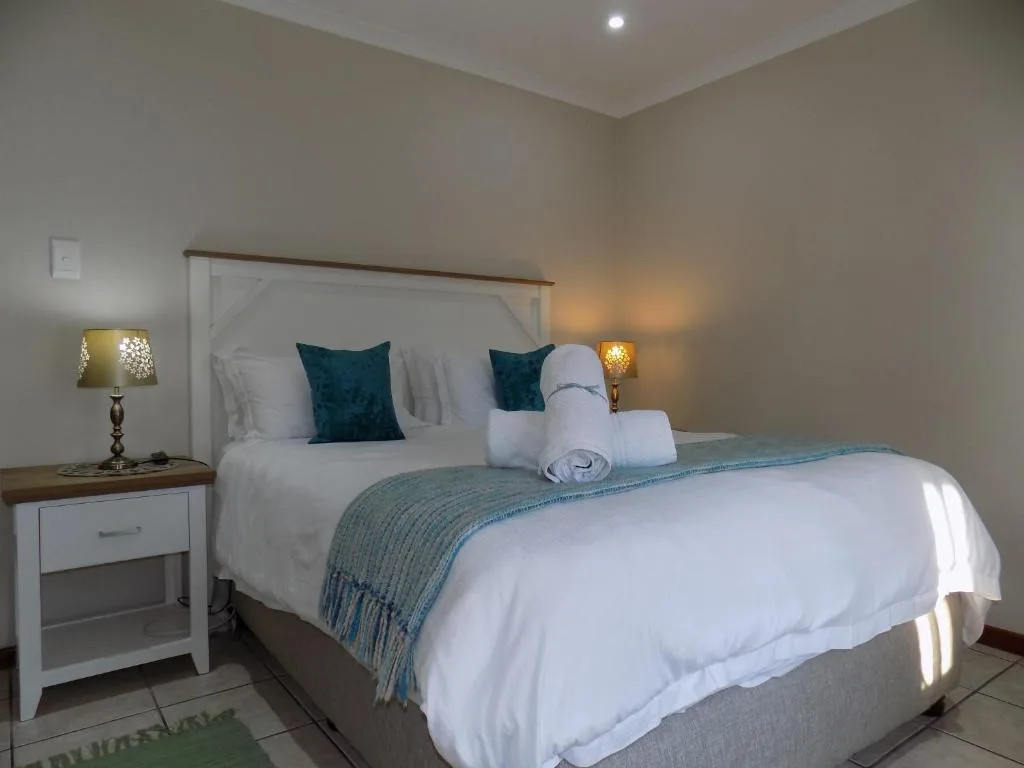 Bright bedroom with queen bed, teal pillows, white bedding, and warm lighting