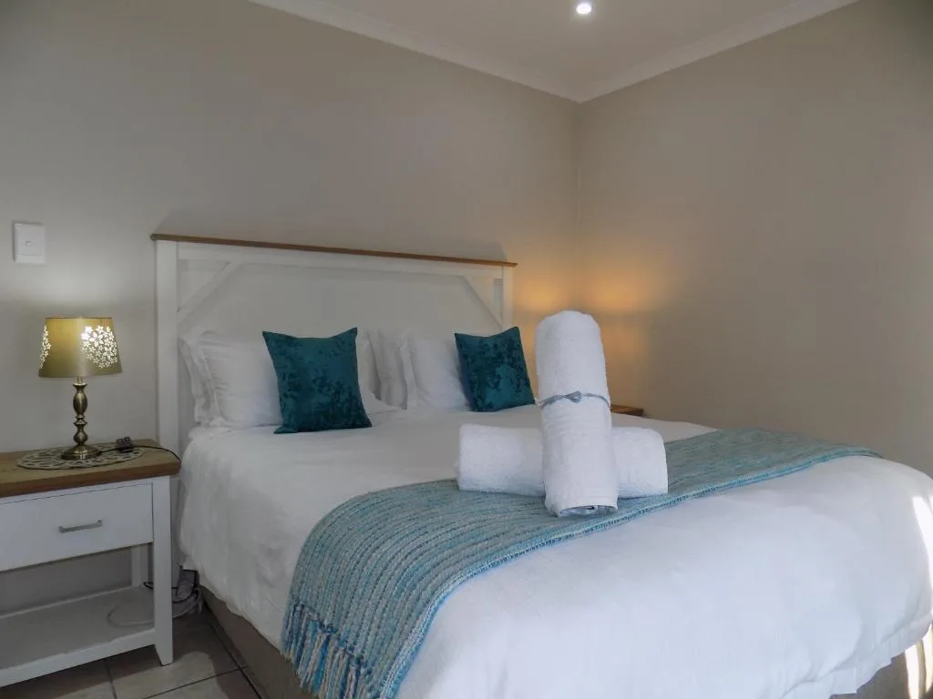 Spacious bedroom with queen bed, teal pillows, white linens, bedside lamp
